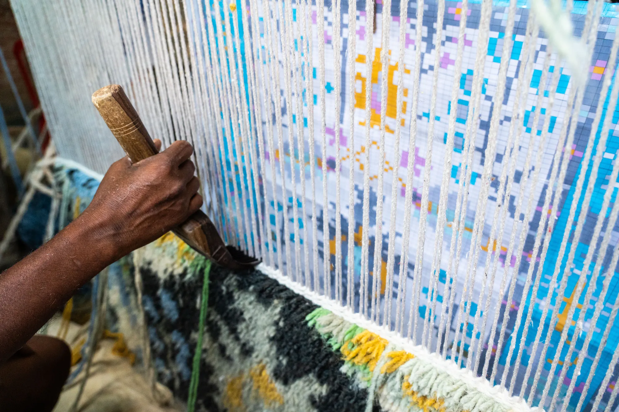 Artisan hand-weaving a rug on a traditional loom.